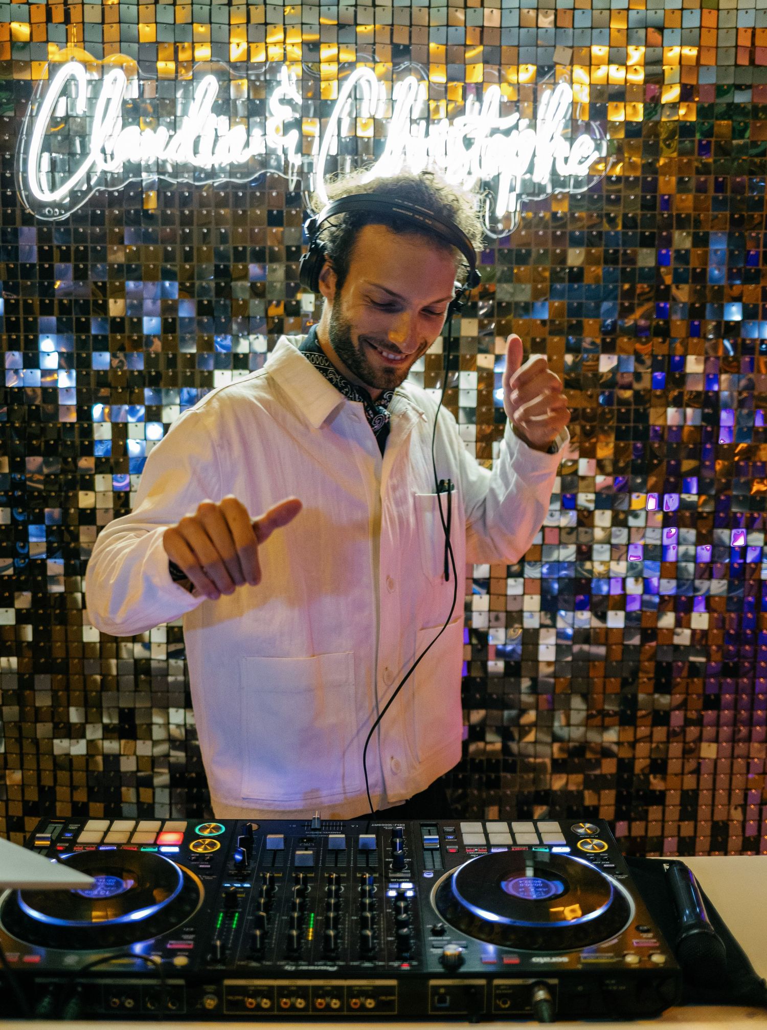 DJ works the turntables and mixer at a nightclub with shimmering disco tiles in the background.