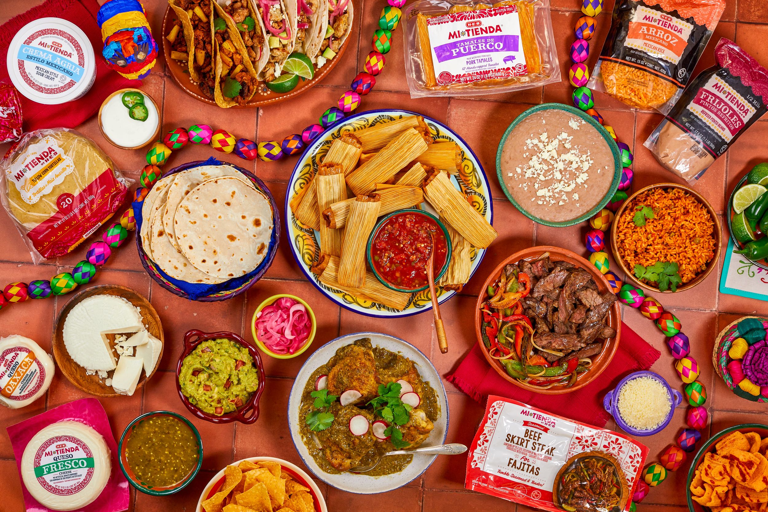 Vibrant overhead view of Mexican food spread including tacos, guacamole, salsas, rice and tortilla chips on a wooden table.