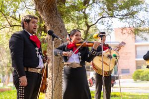 A Mexican mariachi band performs traditional music while playing guitars and violins outdoors under trees.