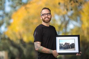 Person in black shirt holds framed artwork outdoors with autumn foliage in background.