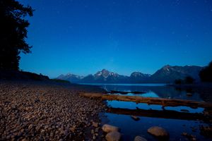 Mountain peaks reflect in pristine lake waters under a deep blue sky at Grand Teton National Park during twilight.