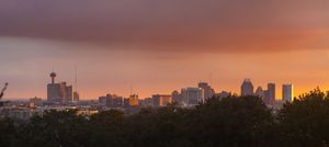 Orange sunset sky illuminates the silhouetted skyline of San Antonio, Texas with downtown buildings.
