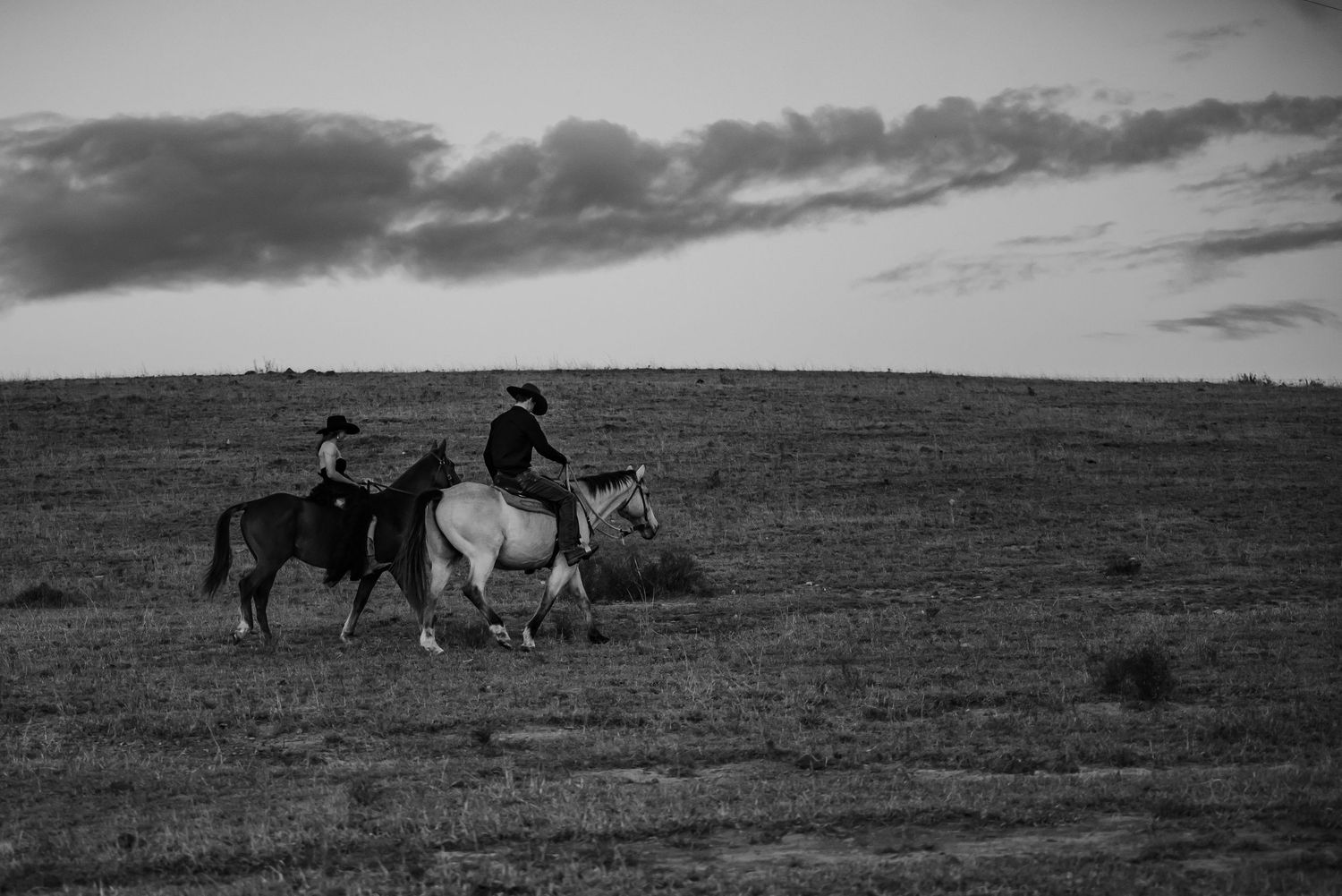 Historical panoramic view of horse riders traversing rugged western terrain under dramatic cloudy skies.