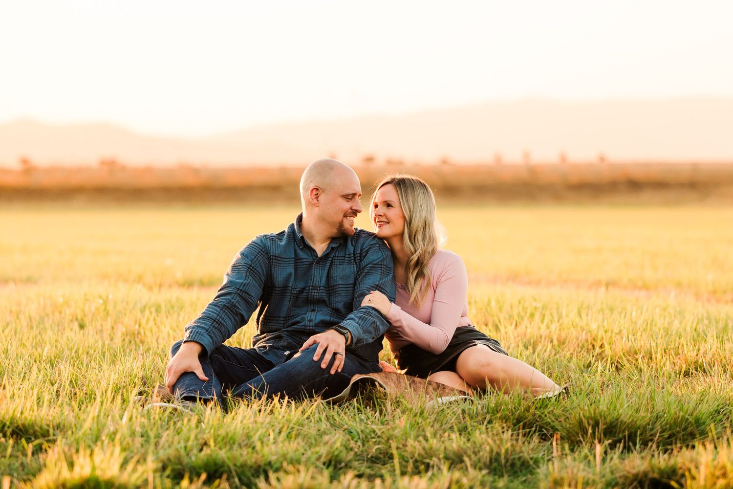 A couple shares an intimate moment on a sun-drenched wheat field during golden hour.