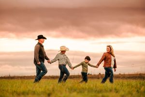 People run holding hands through a golden field at sunset creating a silhouette panorama.