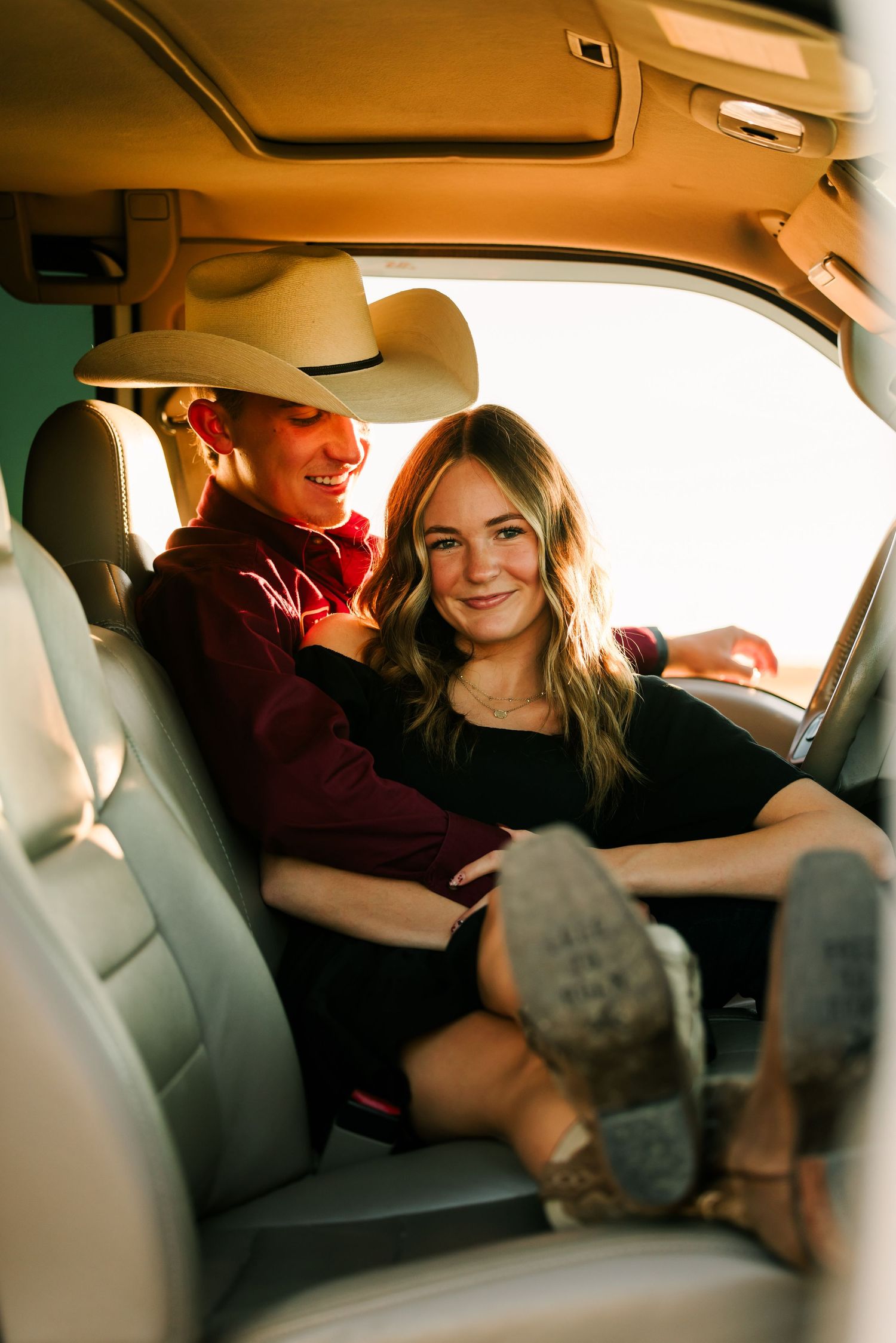 A couple shares a playful moment together in the backseat of a car with warm lighting and comfortable seating.