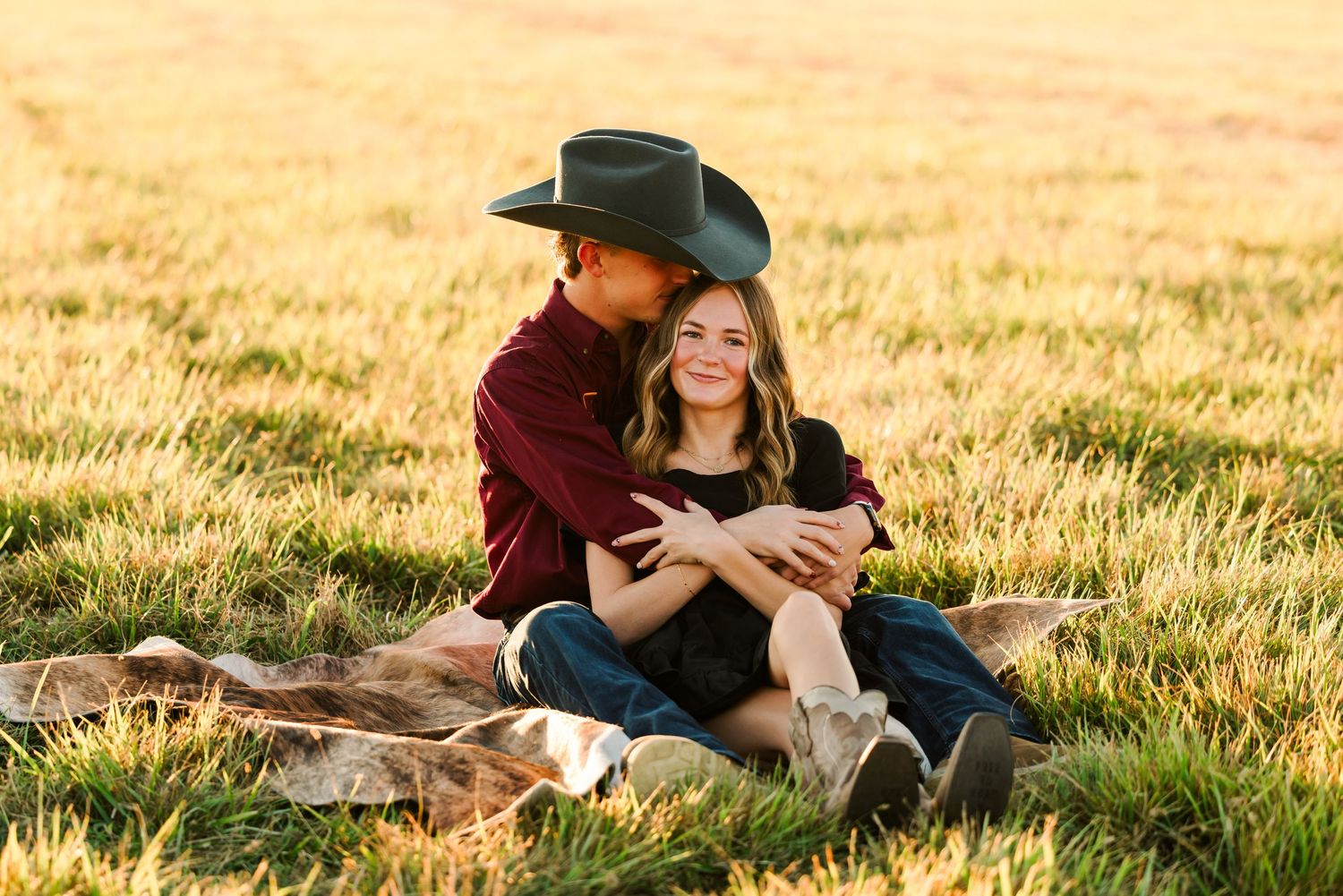 Warm sunset light falls on a couple cuddling in a grassy field during a romantic outdoor photo session.