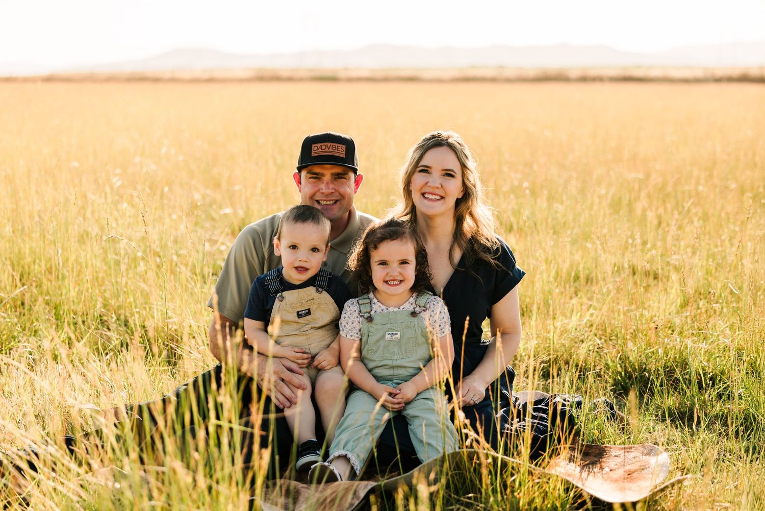 Family sits together in a golden wheat field during sunset creating a warm silhouette against the horizon.