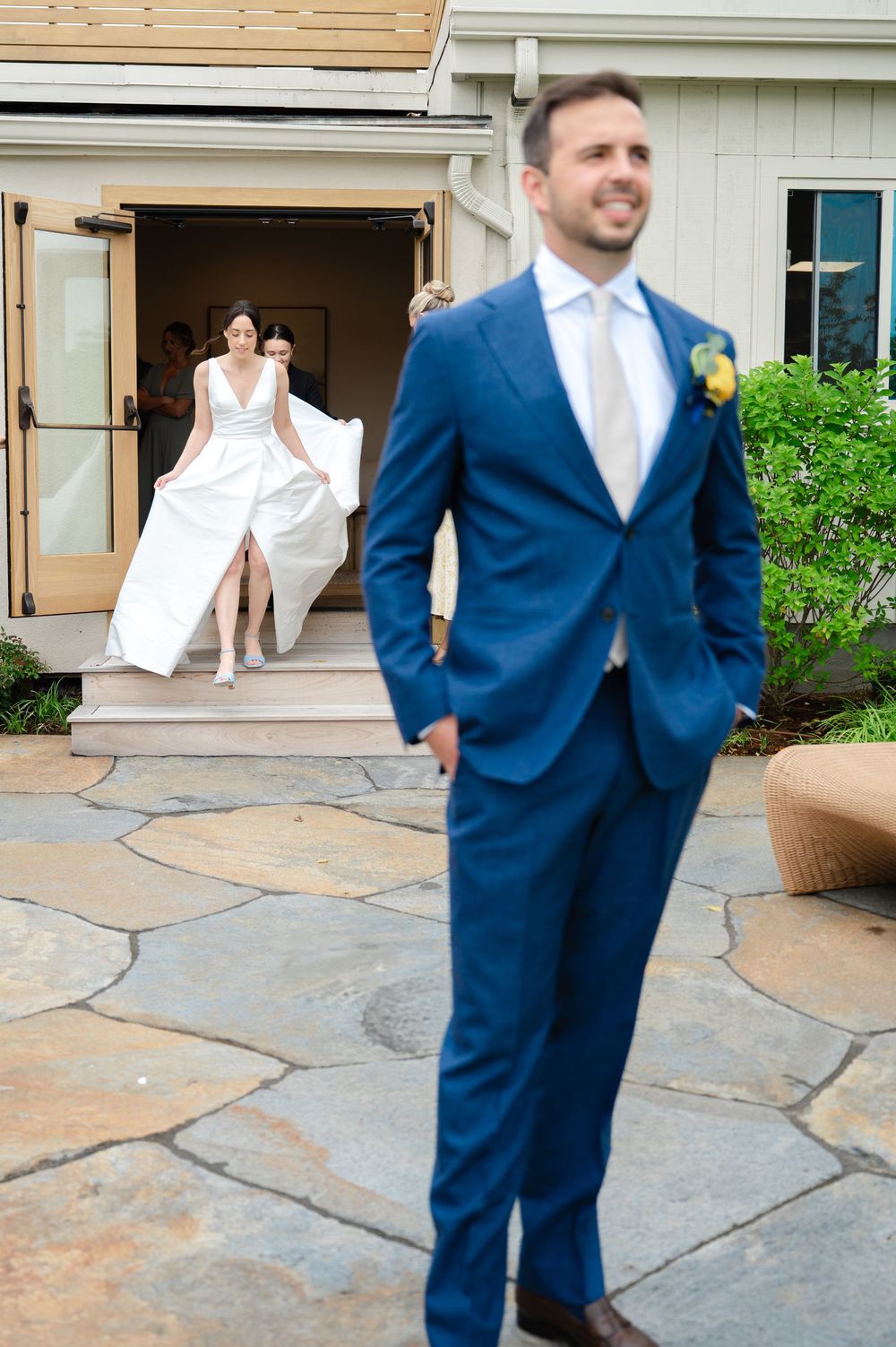 Four connected photos show a playful first look moment featuring a blue suit and white dress on a stone patio.