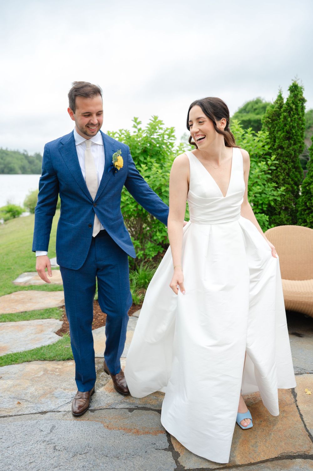 A couple walking on a pathway through greenery in wedding attire with a white dress and navy suit.