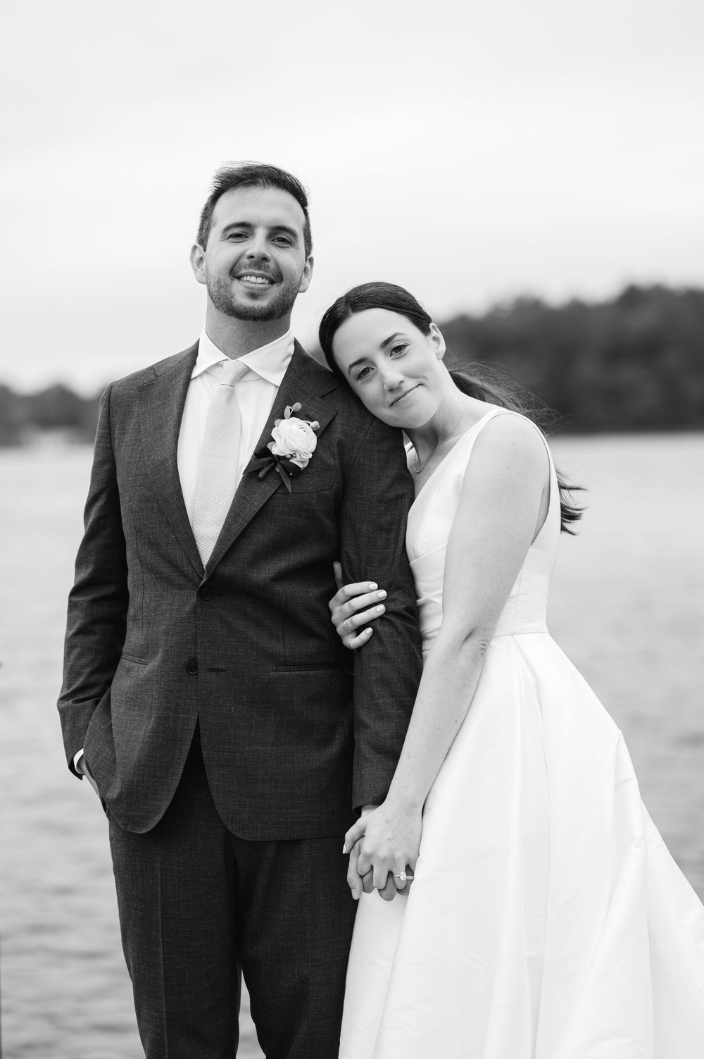 Black and white wedding portrait of newlyweds leaning against each other on the dock of the Lakehouse in Halfiax, MA.