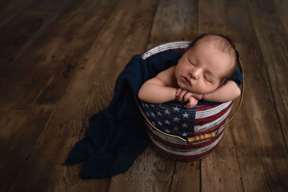 A series of seven similar photos showing a sleeping baby wrapped in an American flag blanket on a wooden floor.