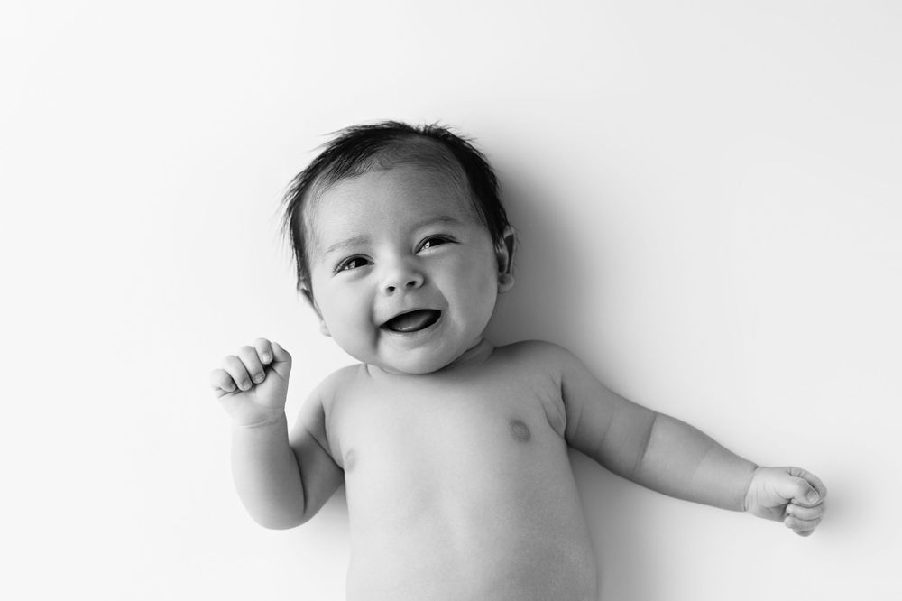 Black and white photo of a happy smiling baby lying on white background with fist raised.