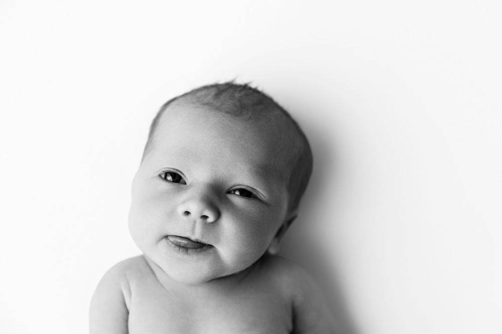 A black and white portrait of a baby looking up with an inquisitive expression.