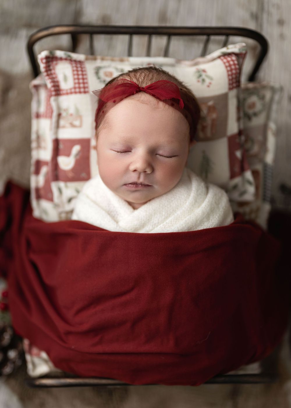 A sleeping newborn baby wrapped in white and red blankets rests peacefully in a rustic wooden basket.
