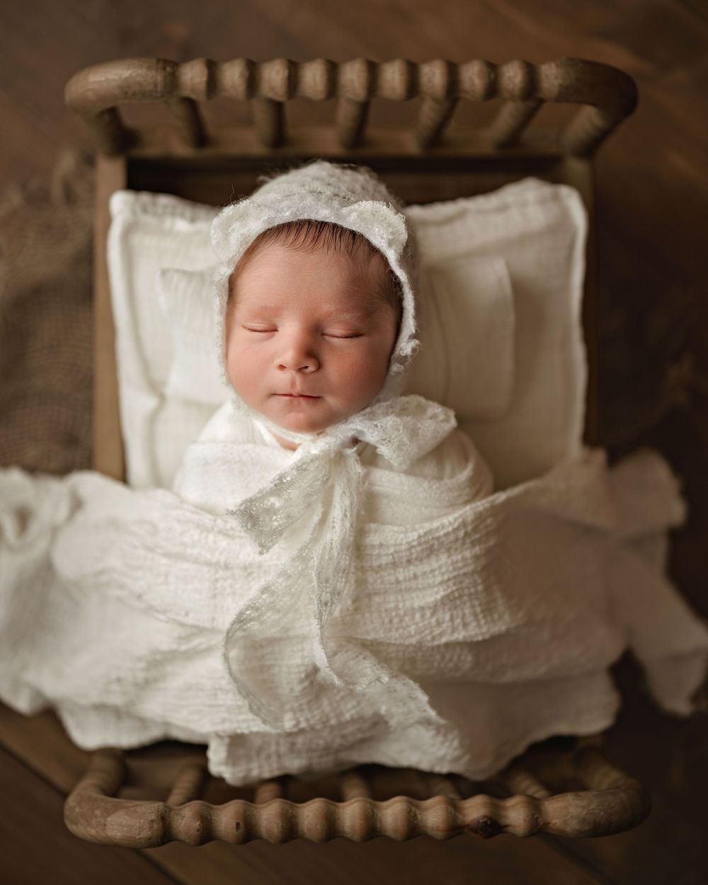 Artistic heritage-style photo series shows a sleeping newborn swaddled in white lacy fabric with vintage spools framing the edges.