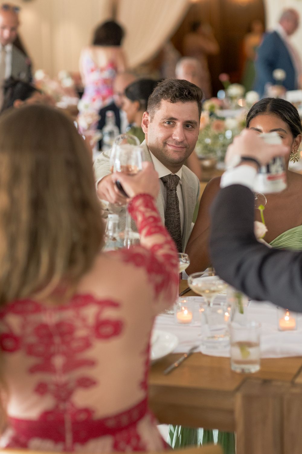 Guests seated at elegant wedding reception tables with candlelight and floral centerpieces in a warm, intimate setting.