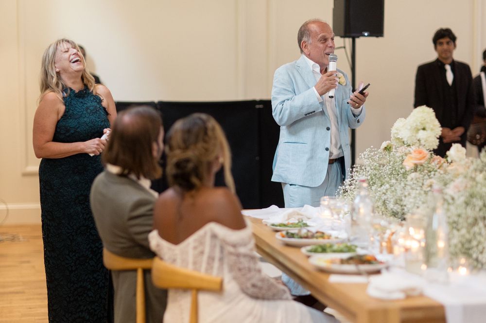 A group of guests celebrating and laughing together during a wedding reception at an elegant indoor venue.