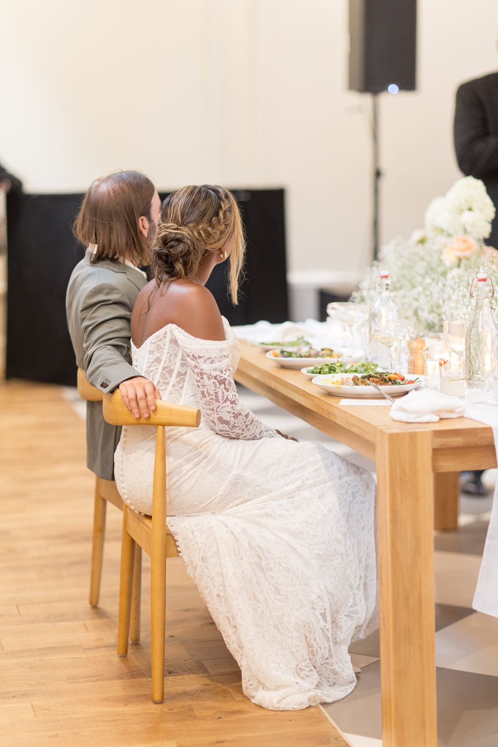 White lace wedding dresses are visible as guests sit at wooden tables during an elegant reception event.