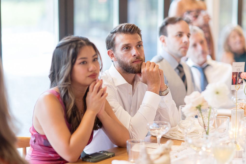 A crowd of wedding guests reacts emotionally during a reception speech while seated at tables.