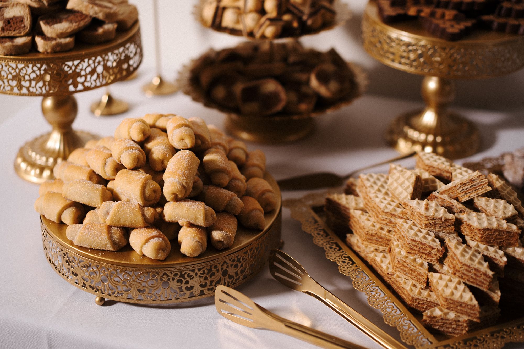Elegant display of cookies and pastries arranged on decorative gold cake stands at a dessert table.