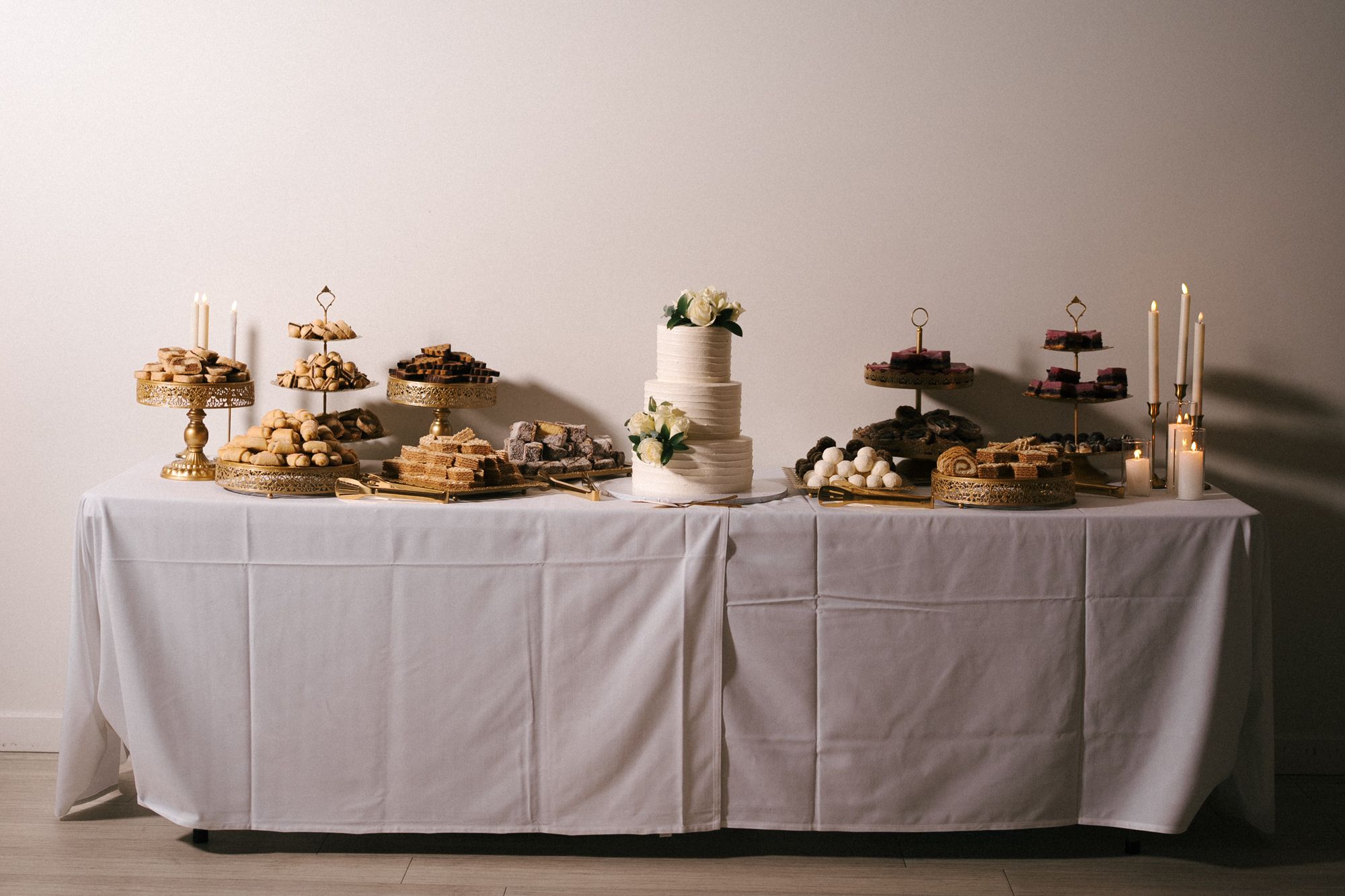 A long white wedding reception table decorated with elegant flowers, candles and plates in a rustic venue setting.