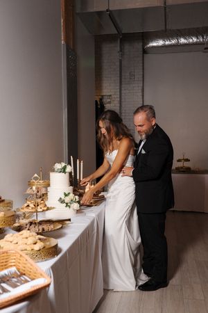 Four sequential images show a couple setting up and arranging their wedding dessert table in an elegant indoor venue.