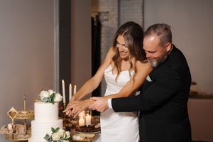 A bride and groom cut their white wedding cake together at an elegantly decorated reception table with candles and flowers.