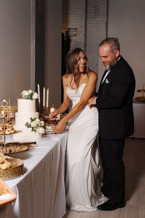 A couple in formal wedding attire cutting their white wedding cake together at an elegant reception.