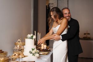Newlywed couple cuts their elegant white wedding cake together at their reception dessert table decorated with flowers.