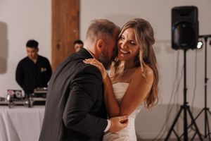 Guests enjoy dancing and mingling at an indoor wedding reception with warm lighting and wooden beams.