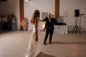 Dancing at wedding reception with DJ speakers and wood beam visible in industrial-style venue.