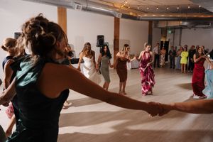 A group of celebratory guests dancing together on a dance floor at an indoor event space with string lights above.
