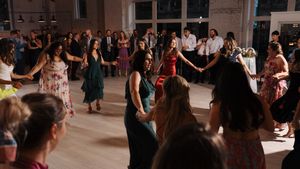 A large group of wedding guests dancing together in a circle on a spacious dance floor at a reception venue.