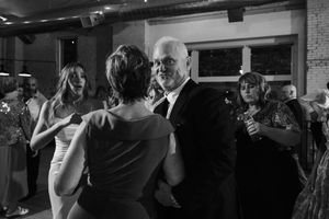 Black and white photo of people dancing together at an indoor social event or celebration.
