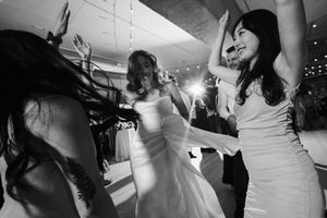 People dance and celebrate during a wedding reception in black and white with festive lighting.