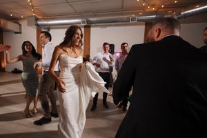 Wedding guests dance and celebrate on a warm-lit rustic wooden dance floor at an indoor reception venue.