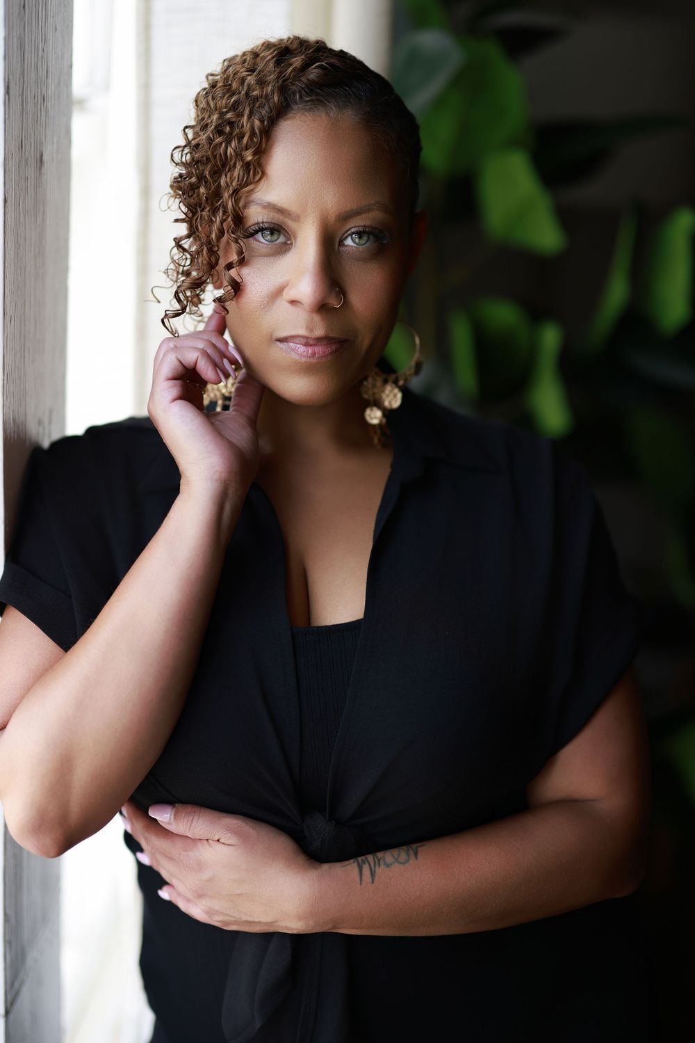 Professional portrait of person with curly hair wearing black top by window.