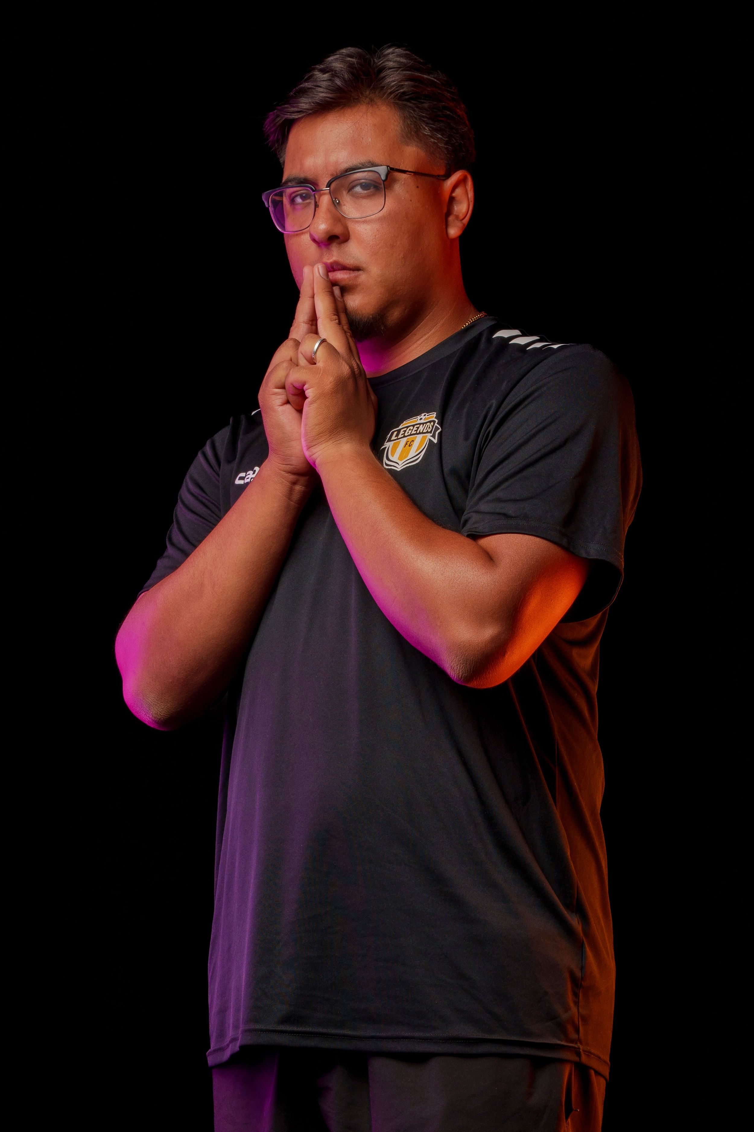Coach makes hushing gesture in dramatic lighting against dark backdrop.