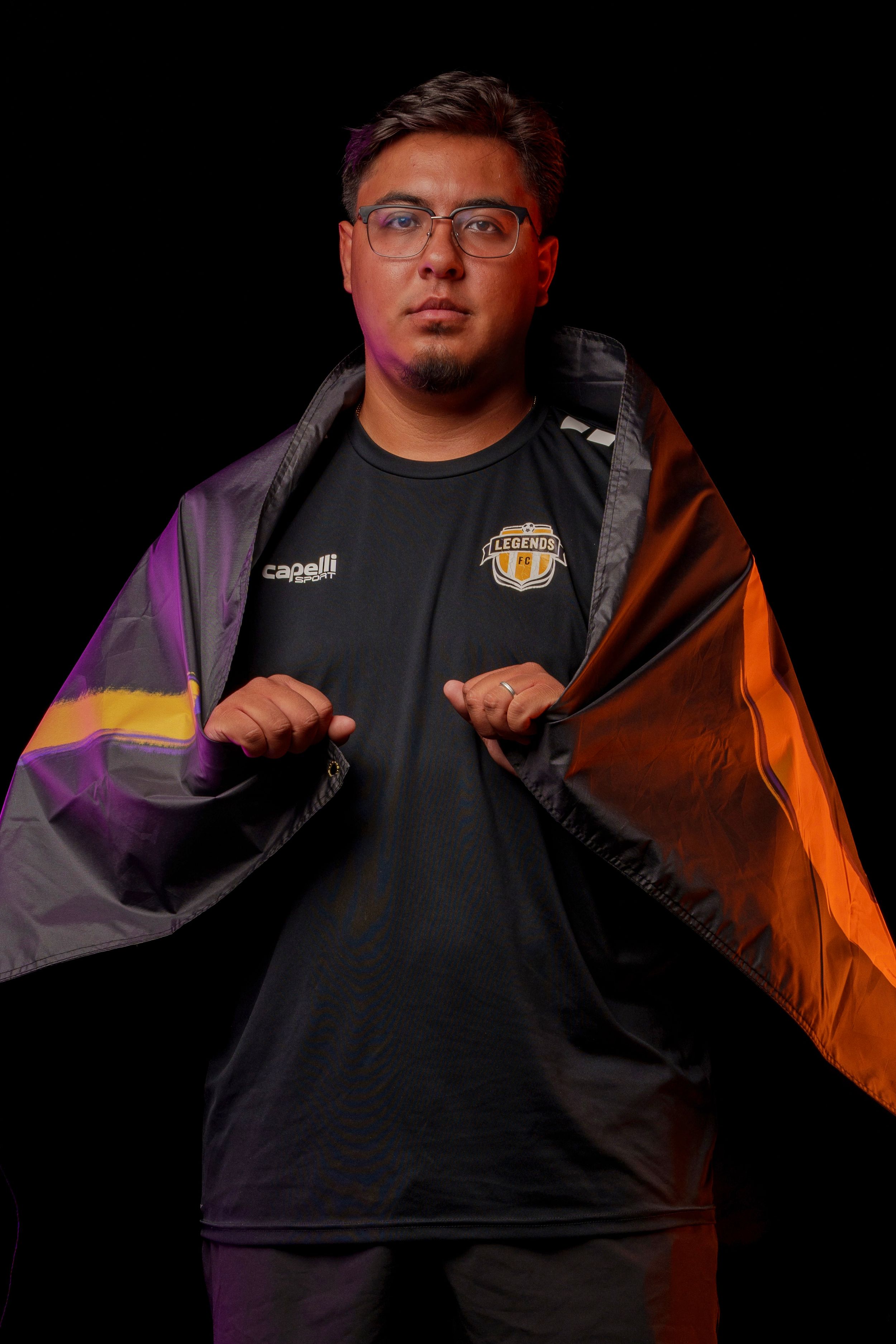 Soccer coach poses dramatically in dark uniform with colorful lighting effects.