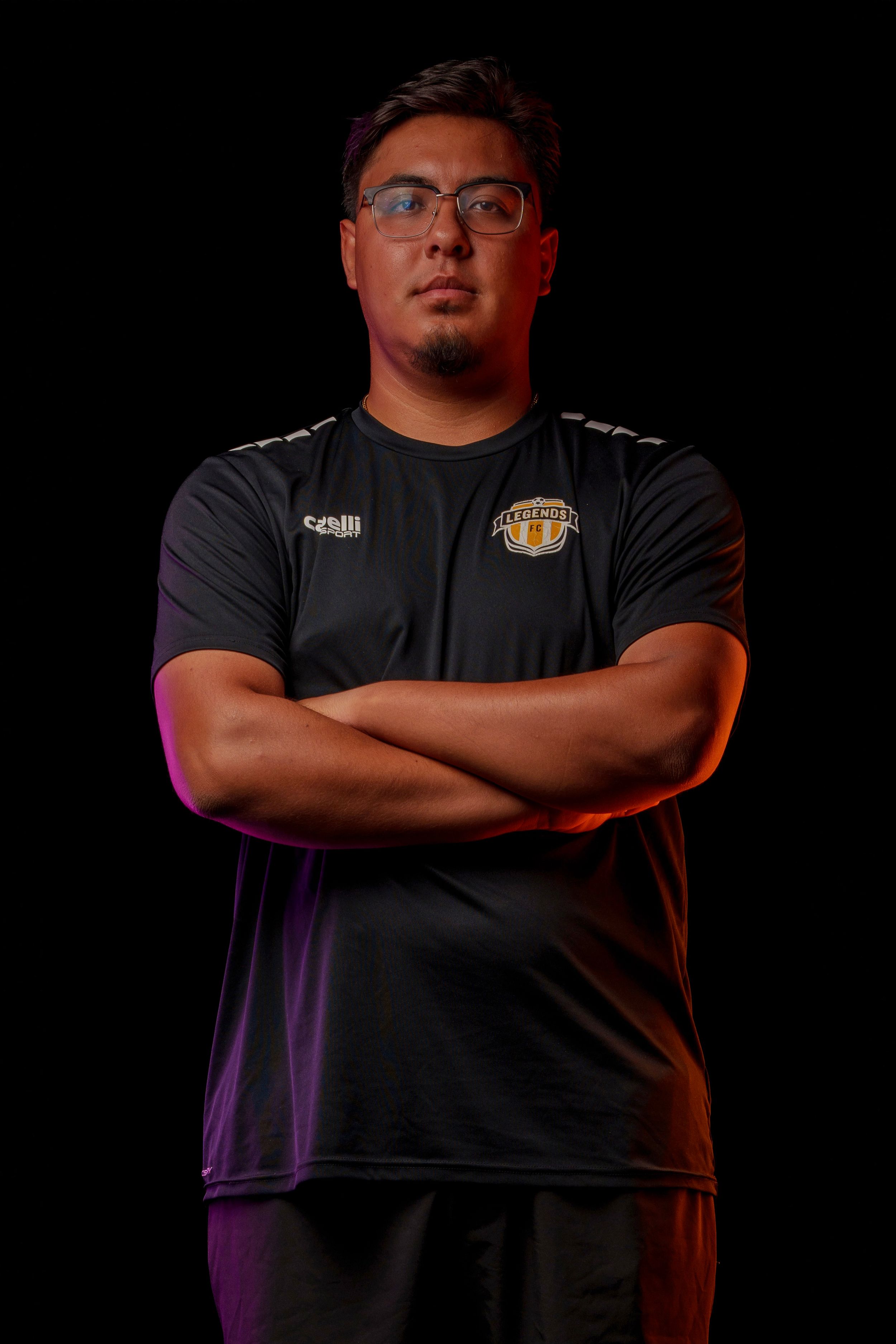 Soccer coach poses with crossed arms in dramatic lighting against dark background.