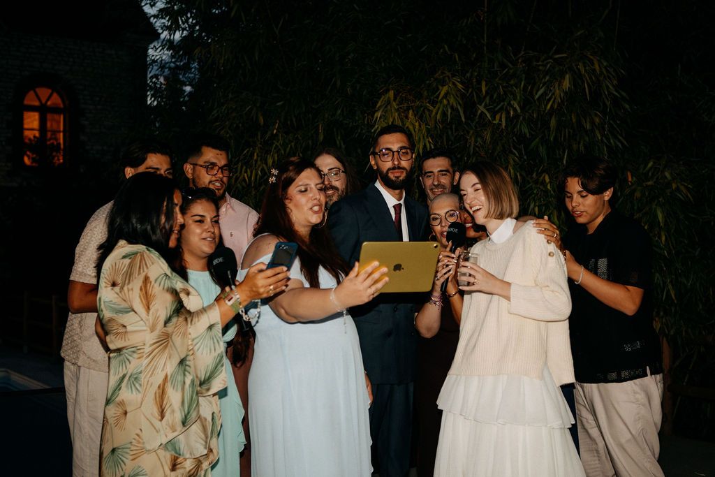 A group of wedding guests gather together for a joyful nighttime selfie at an outdoor reception.