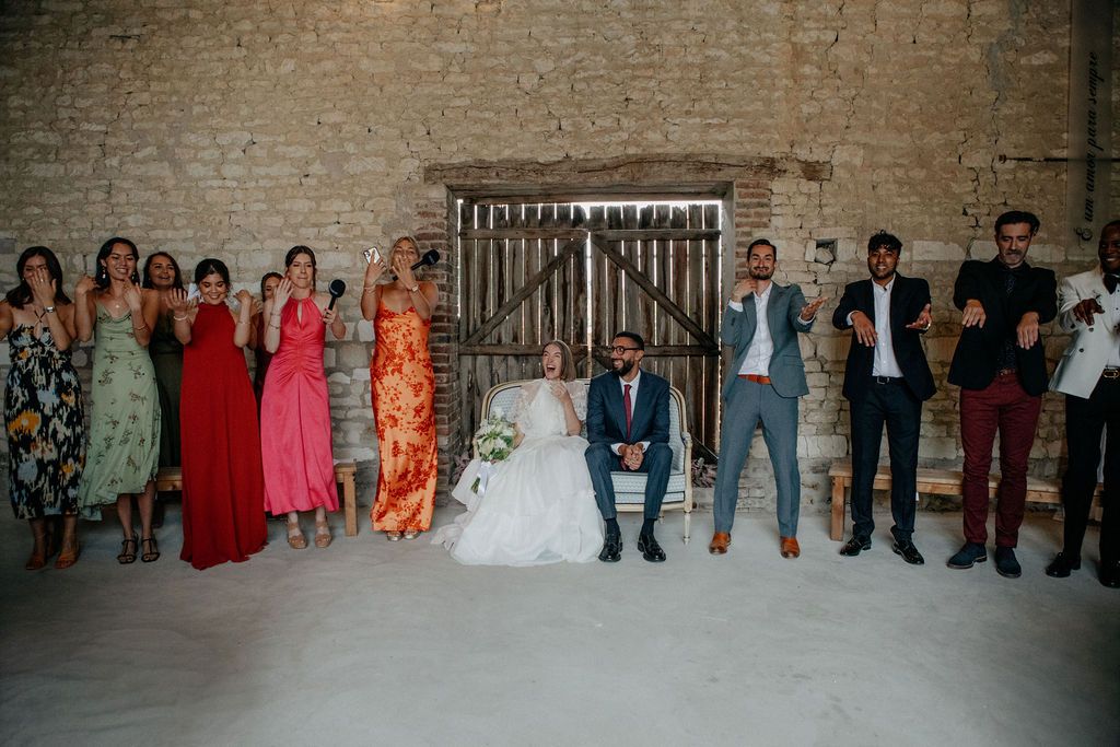 Bride and groom seated with wedding party celebrating inside rustic stone barn venue.