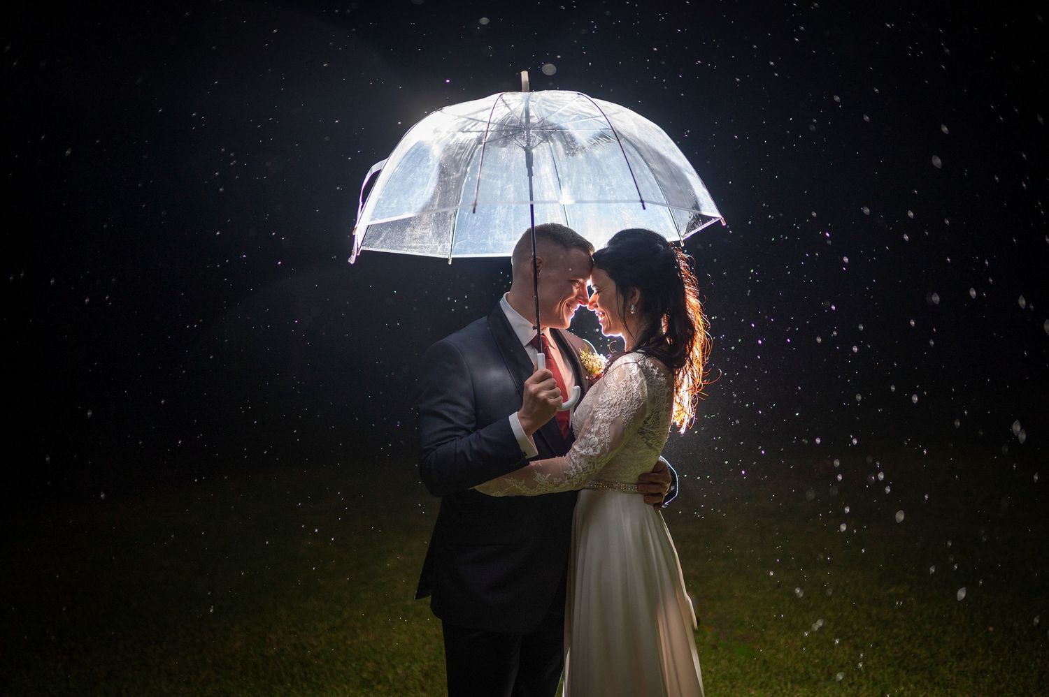 A couple shares an intimate moment under a white umbrella at night with rain and dramatic lighting.