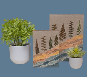 Modern home decor featuring potted plants and nature-inspired journals with fern silhouettes against a blue backdrop.