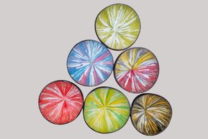 Vibrant watercolor bowls in red, yellow, blue and brown create an abstract spin art pattern on white background.