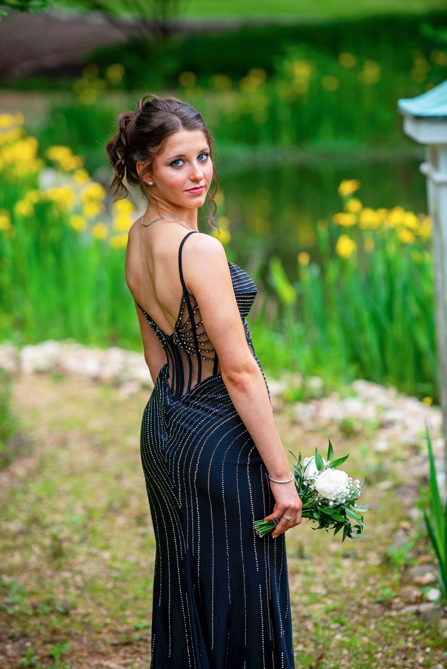 Elegant figure in navy beaded dress poses in garden with bouquet.