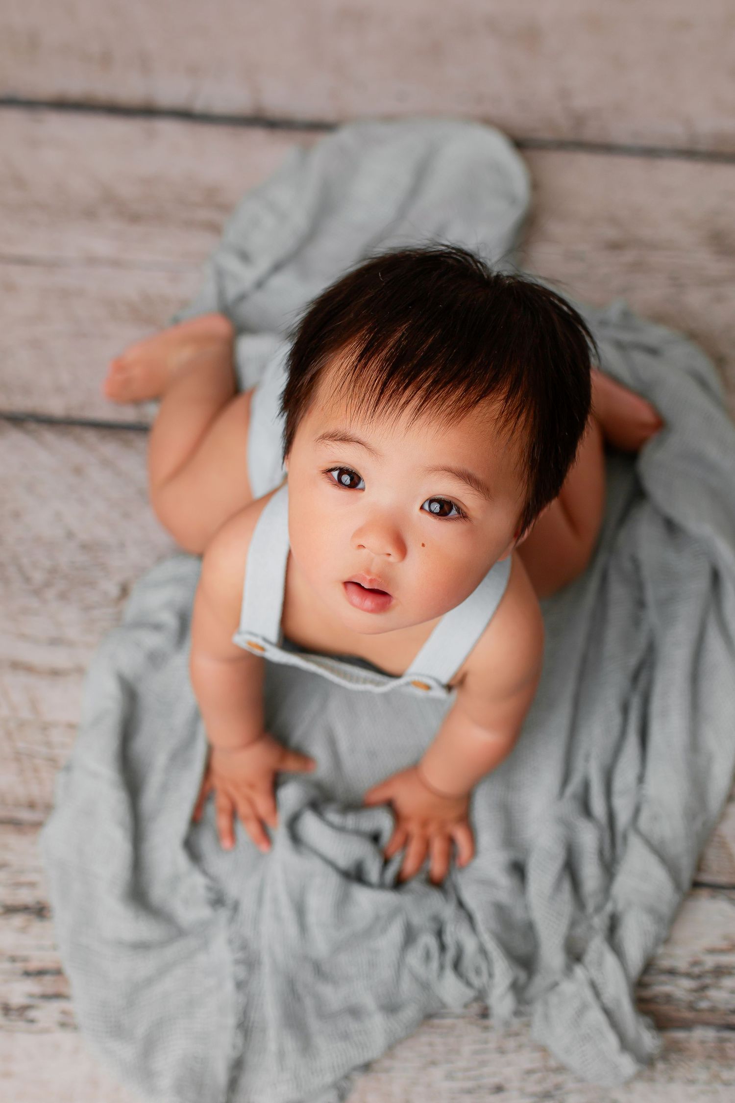 Baby boy in blue romper looking up during milestone sitter session at Flowertown Photography in Summerville SC