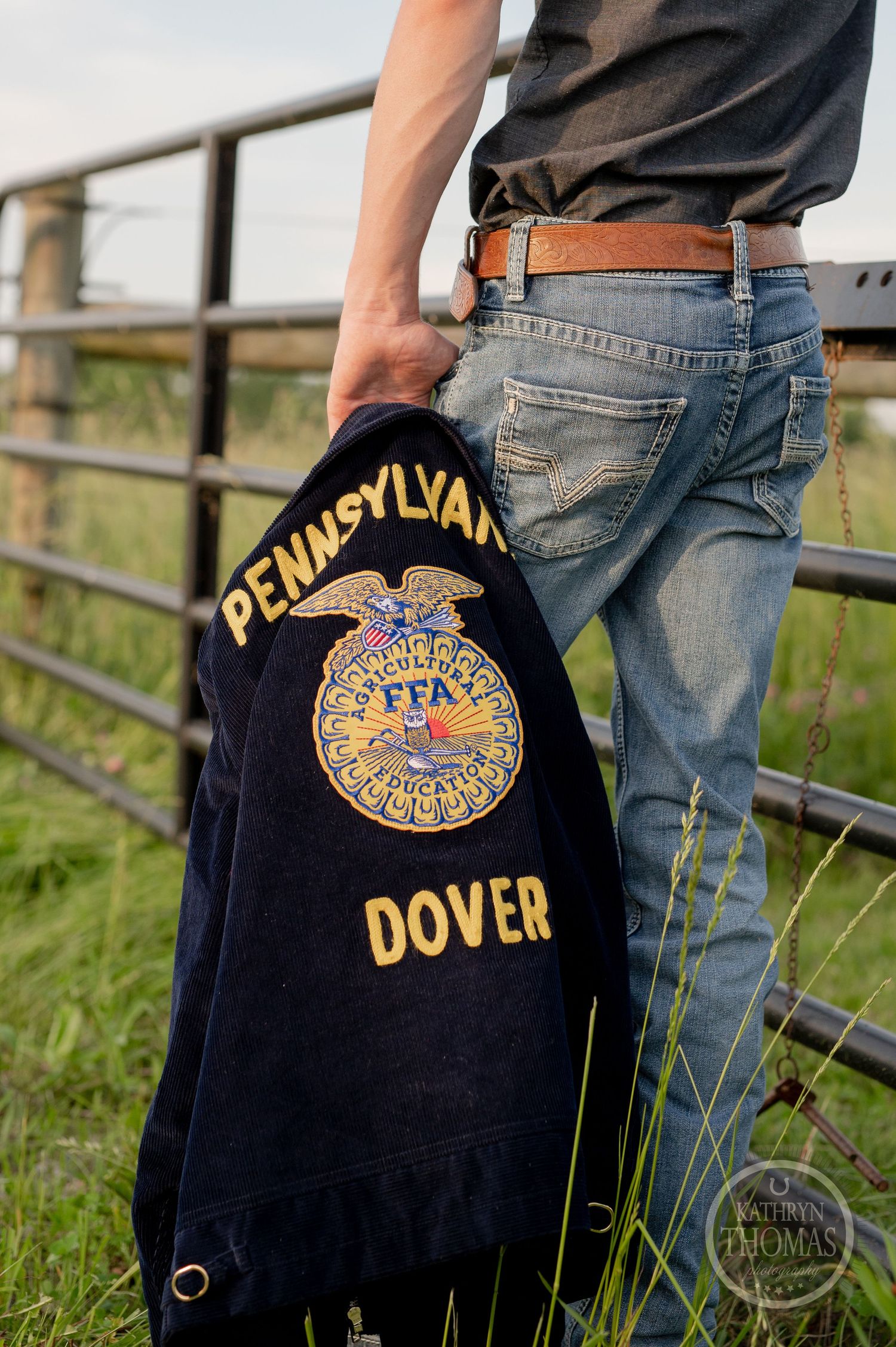Close-up of Pennsylvania Dover FFA jacket emblem and jeans against metal fence.