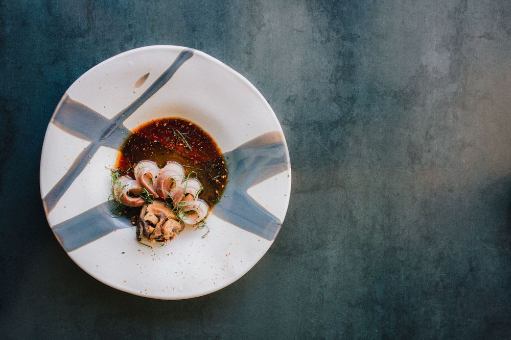 Artistic plating of seafood in dark sauce on geometric patterned white plate.